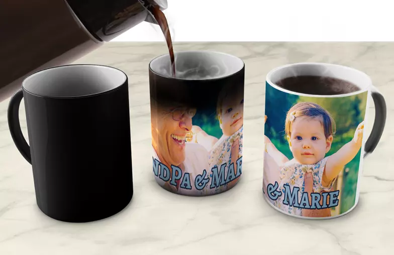 Magic Mug|Three mugs, being filled with hot water to reveal a baby.|Young boy holding custom designed magic mug with photo of himself on|Magic mug with picture of cat on having tea poured into it on desk|Couple holding two heat changing magic mugs with custom text by Printerpix|Three mugs: one empty (blank), one half full (half an image) and one full (full image)|Grandad and grand daughter holding hands with personalised mug with photo of grand daughter||||